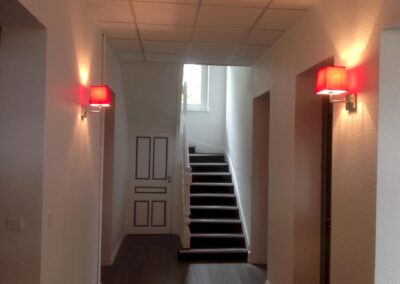 Couloir et cage d’escalier du cabinet d’avocats, avec éclairage mural et câbles intégrés dans les faux plafonds pour préserver l’esthétique