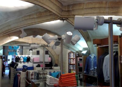 Intérieur du magasin de vêtements sous voûtes en pierre apparente, éclairage sur rails orientables soulignant les volumes et les rayonnages