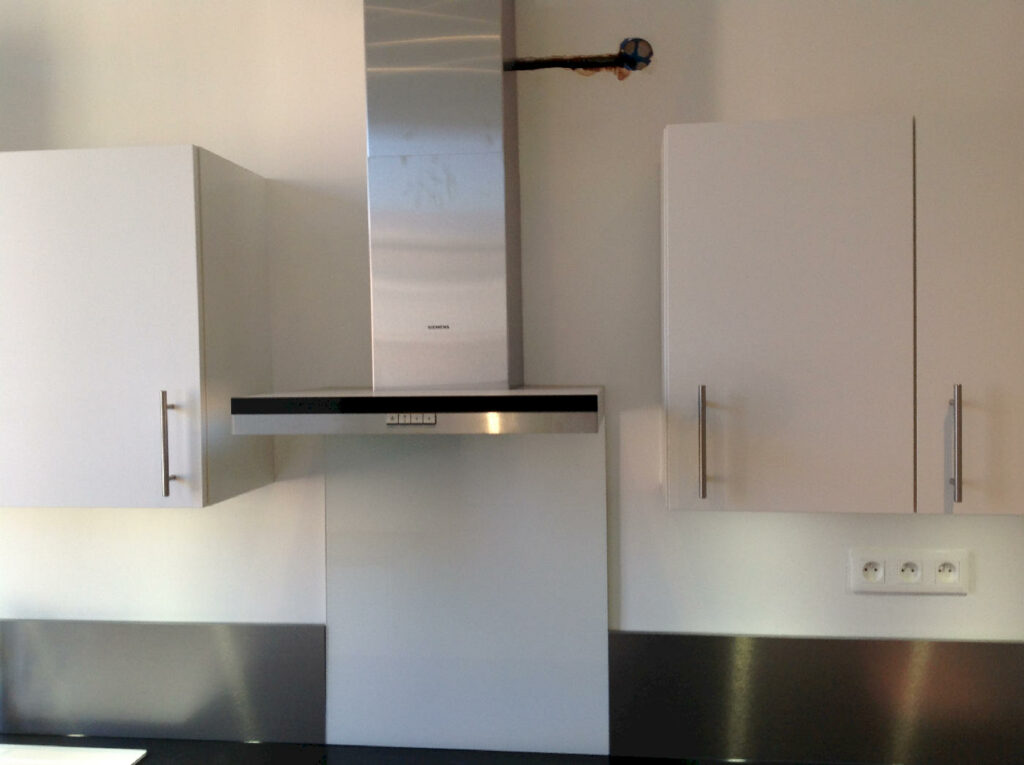 Mur de cuisine équipé d’une hotte inox, de meubles hauts et d’appareillages électriques neufs, dans un appartement entièrement remis à neuf