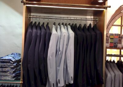 Présentoir de costumes homme dans un magasin de vêtements, éclairé par des spots intégrés au mobilier pour mettre les vestes en valeur