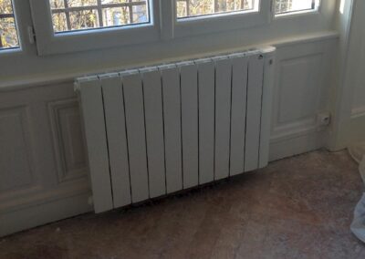 Radiateur électrique moderne installé sous fenêtre dans un appartement rénové, finitions soignées des habillages muraux et menuiseries
